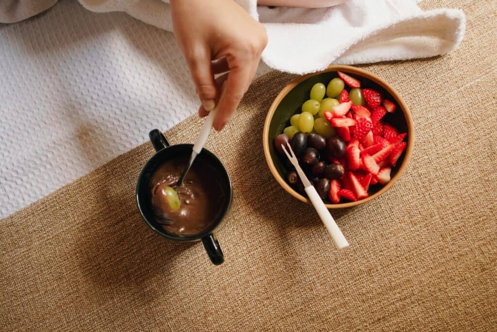 A Person Dipping Fruits in the Cup with Chocolate