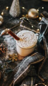 A glass with a white frothy drink and a cinnamon stick in it