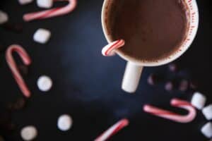 A white mug containing a brown drink with candy canes on a black table