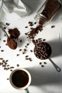 coffee beans beside a white ceramic mug and stainless steel spoon